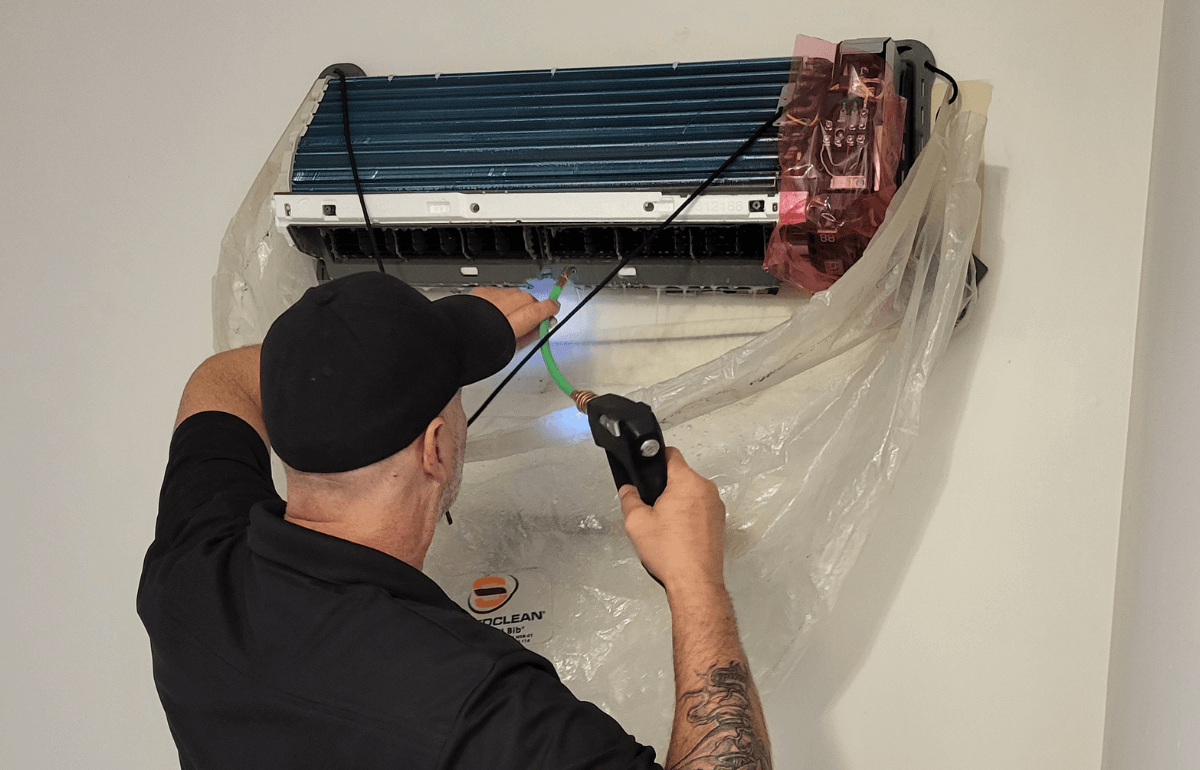 Technicien effectuant le nettoyage intérieur d’un climatiseur mural à l’aide d’un équipement spécialisé.